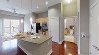 Located at 154–198 S Dawson Street in downtown Raleigh, NC, this single-floor residence combines contemporary design with functional living spaces. The open-concept kitchen and living area serves as the heart of the unit, anchored by a generous granite-topped island with an undermount sink and pendant lighting overhead. Light maple cabinetry lines the kitchen walls, complemented by a full suite of stainless steel appliances, including a side-by-side refrigerator with ice maker, gas range, and built-in microwave. Rich hardwood floors extend throughout the main living area, which benefits from soaring ceilings and a ceiling fan. Sliding glass doors open onto a private balcony, allowing natural light to fill the space and offering views of the surrounding urban streetscape. The bedroom features soft carpeting, a wide closet with wire shelving, and a large window with city views, creating a bright and restful retreat. The full bathroom is finished with tile flooring, a granite vanity with wood cabinetry, and a tiled tub-shower combination, reflecting a consistent use of quality materials throughout the unit.