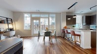 This thoughtfully designed single-floor residence showcases a contemporary aesthetic with a cohesive blend of warm wood tones, neutral walls, and modern finishes throughout. The open-concept layout seamlessly connects the kitchen, dining, and living areas, creating a spacious and functional flow.

The kitchen is outfitted with rich dark wood cabinetry, light stone countertops, a classic tile backsplash, and a full suite of stainless steel appliances. A peninsula with bar seating extends into the dining area, where large windows and a glass-panel door flood the space with natural light and provide access to an outdoor area. Warm hardwood flooring runs throughout the main living spaces, enhancing the inviting atmosphere.

The living room offers a comfortable, well-proportioned space featuring hardwood flooring, a round mirror accent, and generous wall space for artwork. Two bedrooms are carpeted for comfort, each benefiting from natural light through well-sized windows with exterior views. The bathroom features large-format tile flooring, dark wood cabinetry with a stone-topped vanity, and a broad mirror above the sink, reflecting a clean and modern design sensibility throughout the residence.
