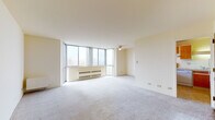 Located in Cudahy, Wisconsin, this single-floor unit offers a well-designed, open layout with neutral tones and plush carpeting throughout the living and bedroom areas. The expansive living room is a standout feature, boasting floor-to-ceiling corner windows that flood the space with natural light and provide pleasant outdoor views. A ceiling fan adds comfort, and baseboard heating units are positioned along the window walls for year-round climate control. The kitchen is thoughtfully laid out with a pass-through counter that opens to the living area, warm wood cabinetry, light countertops, an electric range with overhead exhaust hood, a dishwasher, and a refrigerator — providing ample storage and functionality. The bedroom is generously sized, featuring soft carpeting and a sliding wood-panel closet that offers practical storage space. The bathroom is clean and straightforward, finished with white subway tile surrounding a full tub and shower, a wood-vanity with a single sink, a large mirror, and tile flooring. Throughout the unit, the light, neutral color palette and abundant natural light create a calm and inviting atmosphere.