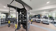 Located at 20350 North 7th Avenue in Phoenix, AZ, this fitness center offers a thoughtfully designed exercise space that accommodates a wide variety of workout styles and fitness goals. The single-floor layout is generously proportioned, providing ample room to move freely between dedicated training zones without feeling crowded.

The cardio section features a row of Life Fitness treadmills equipped with individual digital screens, accompanied by cycling bikes and rowing machines. Large windows along the perimeter flood the space with natural light, while full-length wall mirrors enhance the sense of openness and allow users to monitor their form throughout their workout.

The strength and functional training area is equally well-appointed. A central TRX suspension training rig serves as the focal point, surrounded by a multi-tiered rack stocked with medicine balls, slam balls, and foam rollers. Additional equipment includes a full dumbbell rack spanning a wide weight range, a power rack with a weight plate tree, an adjustable workout bench, and a plyo box for functional training exercises.

The interior design is clean and modern, with white walls, recessed lighting, and a neutral carpeted floor accented by light tile border zones. Potted plants add a touch of greenery throughout the space. The overall ambiance is bright, professional, and motivating — reflecting a facility designed to support a comprehensive fitness experience.