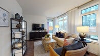This thoughtfully designed single-floor residence offers a seamless blend of modern aesthetics and functional living. The open-concept kitchen is a standout, featuring two-tone cabinetry with white uppers and dark espresso lowers, quartz countertops, a subway tile backsplash, a peninsula island with a stainless steel sink, and a full suite of stainless steel appliances including a French door refrigerator, range, microwave, and dishwasher. Pendant lighting adds a polished finishing touch overhead. The adjacent dining area benefits from expansive floor-to-ceiling windows that flood the space with natural light and offer views of the surrounding urban landscape. The living room is generously proportioned, anchored by large windows with sheer drapery and direct access to a private balcony. Wood-look flooring flows throughout the main living areas, adding warmth and continuity. The primary bedroom opens directly to the balcony through sliding glass doors, while the secondary bedroom features a wall-mounted mini-split unit and a bright outlook window. Both bathrooms are finished with dark wood vanities, white quartz counters, and tiled tub-shower combinations. One bathroom conveniently houses a stacked in-unit washer and dryer. A warm wood-toned entry door completes this well-considered residence.