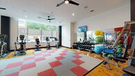 Located at 1916 Addison St in Berkeley, CA, this fitness center is a comprehensively outfitted single-floor space designed to support a wide range of workout routines. The layout is thoughtfully organized to maximize usability, with distinct zones for cardio, strength training, and functional fitness.

Large floor-to-ceiling windows along the street-facing wall flood the interior with abundant natural light while providing views of the surrounding neighborhood streetscape. Ceiling fans throughout help maintain a comfortable environment during workouts. The flooring combines polished hardwood with interlocking red and gray foam mat tiles, delineating workout zones while providing cushioning for high-impact activity.

The cardio zone features treadmills, ellipticals, stationary bikes, and rowing machines. A dedicated strength area includes a multi-station cable machine anchored by a bold red accent wall, a full rack of dumbbells, and an assortment of exercise balls and resistance accessories. Floor-to-ceiling mirrors line one wall, enhancing the sense of space and allowing users to monitor their form. Multiple wall-mounted flat-screen televisions are positioned throughout for entertainment. Recessed lighting and ceiling fans complete the clean, modern aesthetic of this well-appointed fitness facility.