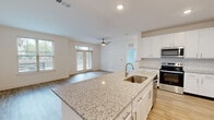 Located at 34 Silverado Circle in Hoschton, GA, this well-designed single-story home offers a thoughtful layout that maximizes comfort and functionality. The open-concept kitchen and living area serves as the heart of the home, anchored by a large granite-topped island with an undermount sink and stylish brushed nickel fixtures. White shaker cabinetry lines the kitchen walls, complemented by a classic subway tile backsplash and a full suite of stainless steel appliances, including a range, over-the-range microwave, and refrigerator. Light wood-style flooring flows throughout the main living areas, enhancing the home's bright, airy feel. The living room is bathed in natural light through multiple windows and French doors that open to the outdoors, with a ceiling fan adding both style and comfort. The bedroom features plush carpeting, a large window with outdoor views, and access to a generous walk-in closet outfitted with extensive wire shelving and hanging rods for ample storage. The full bathroom continues the home's cohesive design with granite countertops, white cabinetry, a framed mirror, and a glass-enclosed shower. Clean white walls and recessed lighting throughout lend the entire space a fresh, modern ambiance.