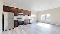 Located at 6916 Fulton St in San Diego, CA, this single-floor unit offers a clean, modern design with a bright and open layout. The interior is finished with light gray hardwood-style flooring that runs throughout, complementing the neutral warm-toned walls and white trim for a cohesive, contemporary aesthetic.

The kitchen serves as a central feature of the space, equipped with rich dark-walnut cabinetry, white countertops, and a full suite of stainless steel appliances including a refrigerator, electric range, built-in microwave, and dishwasher. A single-basin sink is positioned beneath a window that draws in natural light and offers exterior views of the surrounding neighborhood.

The kitchen opens directly into a generously sized living area, creating a seamless open-concept flow. Large windows on multiple walls flood the living space with abundant natural light throughout the day, enhancing the sense of openness and airiness.

A separate room provides additional flexible living space, also featuring a large window with neighborhood views and recessed lighting. The bathroom is finished with a dark-wood vanity, white quartz countertop, an undermount sink with a brushed nickel faucet, and a large frameless mirror. Recessed lighting is present throughout the unit, adding to the clean, modern feel of the overall space.