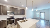 This single-story residence in Gulf Breeze, Florida offers a thoughtfully designed open-concept layout that seamlessly connects the kitchen, dining, and living areas. The kitchen is a standout feature, showcasing rich dark-toned cabinetry with sleek hardware, bright white quartz countertops, and a full suite of stainless steel appliances including a refrigerator, range, and built-in microwave. A central island with an undermount sink and pendant lighting above serves as both a functional workspace and a natural gathering point. Light wood-style flooring runs throughout the main living areas, complementing the neutral color palette and contributing to an airy, modern aesthetic. The living area benefits from natural light through windows with blinds and is finished with a ceiling fan. The bedroom is carpeted for comfort and features a walk-in closet with built-in shelving, providing generous storage. The bathroom includes a soaking tub with shower, wood-look tile flooring, and clean white finishes. A dedicated laundry area with washer and dryer hookups and additional shelving adds practical convenience to this well-appointed residence.