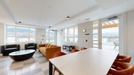 This 440 square foot space in Kelowna, BC, offers a versatile and contemporary setting. The open-concept design seamlessly integrates living, dining, and entertainment areas. Floor-to-ceiling windows dominate one wall, flooding the space with natural light and providing stunning mountain views. The room features a sophisticated color palette with white walls and a unique checkerboard-patterned floor.

The living area is furnished with a striking mustard-yellow sofa and two charcoal armchairs, centered around a sleek black coffee table. A large dining table with wooden chairs accommodates group gatherings. The kitchenette, tucked along one wall, boasts modern gray cabinetry and a white countertop.

Notable features include a state-of-the-art large-screen TV mounted on the wall, creating an immersive entertainment experience. Underneath, a wooden storage unit adds warmth and functionality. Thoughtful lighting elements, including ceiling-mounted spots and designer wall sconces, enhance the ambiance.

The space's layout and amenities make it ideal for various uses, from casual lounging to hosting social events. Its modern aesthetic, combined with the panoramic views of Kelowna's landscape, creates an inviting and stylish environment.