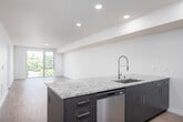 This single-floor residence offers a thoughtfully designed open-concept layout with clean lines and a neutral color palette throughout. Hardwood-style flooring runs continuously across the living and kitchen areas, creating a cohesive and polished aesthetic.

The kitchen is well-appointed with dark cabinetry, granite countertops, a subway tile backsplash, and a full suite of stainless steel appliances, including a refrigerator, range, and microwave. An island with a sink provides additional counter space and facilitates an easy flow into the adjoining living area.

The living space is generously proportioned, featuring a ceiling fan with integrated lighting and large sliding glass doors that open to an outdoor balcony, filling the room with natural light and views of surrounding greenery.

A hallway connects the living areas to the bedrooms and bathrooms, with one bedroom featuring a closet with built-in shelving. The bathroom is cleanly finished with a dark vanity, granite countertop, and a full tub-shower combination with white subway tile surround.

A dedicated laundry area accommodates a full-size washer and dryer, adding practical convenience to the unit's overall functional design.