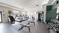 Located at 73 Brownstone Way in Englewood, NJ, this fitness center offers a generously sized, single-floor layout designed to accommodate a wide range of workout needs. The space is defined by its bright, welcoming atmosphere, enhanced by large windows along the perimeter that allow abundant natural light to fill the room throughout the day.

The cardio zone features a row of treadmills, an elliptical, and a stair climber, all positioned to take advantage of the natural light from the surrounding windows. Dedicated rubber flooring in this area provides stability and impact absorption. Adjacent to the cardio section, a comprehensive cable and multi-functional strength machine supports a variety of resistance training exercises, complemented by a full dumbbell rack and flat benches for free weight work.

A stretch and functional training area offers open floor space covered in rubber matting, ideal for bodyweight exercises and cooldowns. A rack stocked with medicine balls, resistance bands, and exercise mats lines one wall, providing versatile training accessories. Full-length mirrors are mounted along one side of the space, supporting form-checking during workouts.

The interior design features a combination of neutral beige tones and a deep green accent wall, crown molding, a tray ceiling with recessed lighting, and wood-look flooring in the open zones — all contributing to a polished, modern aesthetic. Glass-paneled entry doors complete the professional feel of this well-appointed fitness facility.