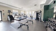 Located at 73 Brownstone Way in Englewood, NJ, this fitness center offers a generously sized, single-floor layout designed to accommodate a wide range of workout needs. The space is defined by its bright, welcoming atmosphere, enhanced by large windows along the perimeter that allow abundant natural light to fill the room throughout the day.

The cardio zone features a row of treadmills, an elliptical, and a stair climber, all positioned to take advantage of the natural light from the surrounding windows. Dedicated rubber flooring in this area provides stability and impact absorption. Adjacent to the cardio section, a comprehensive cable and multi-functional strength machine supports a variety of resistance training exercises, complemented by a full dumbbell rack and flat benches for free weight work.

A stretch and functional training area offers open floor space covered in rubber matting, ideal for bodyweight exercises and cooldowns. A rack stocked with medicine balls, resistance bands, and exercise mats lines one wall, providing versatile training accessories. Full-length mirrors are mounted along one side of the space, supporting form-checking during workouts.

The interior design features a combination of neutral beige tones and a deep green accent wall, crown molding, a tray ceiling with recessed lighting, and wood-look flooring in the open zones — all contributing to a polished, modern aesthetic. Glass-paneled entry doors complete the professional feel of this well-appointed fitness facility.