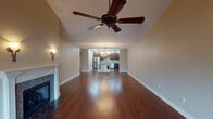 This well-appointed single-floor home blends classic elegance with functional design throughout its thoughtfully laid-out spaces. The expansive main living area immediately commands attention with its vaulted ceiling, rich dark hardwood flooring, and an ornate multi-arm chandelier that anchors the room. A fireplace with a clean white mantle adds warmth and character, while sliding glass doors at the far end invite natural light and outdoor views. This space flows seamlessly into an open living and dining zone, where a ceiling fan with dark wood blades complements the soaring ceiling height.

The kitchen is a standout feature, showcasing deep mahogany cabinetry, granite countertops in earthy tones, stainless steel appliances including a gas range with a sleek overhead hood, and a central island. Recessed lighting and an elegant wall sconce add both function and ambiance. Additional rooms offer hardwood flooring, neutral green-toned walls, and multiple windows that flood the space with natural light.

The bathrooms are finished to a high standard, featuring travertine and marble tile work, cream cabinetry with dark granite vanity tops, tub-shower combinations with decorative tile insets, and framed mirrors. Together, these spaces reflect a cohesive design sensibility combining traditional elegance with modern comfort.