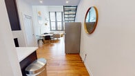 Located in West Philadelphia, this 3-bedroom, 2-bathroom multi-floor unit offers a distinctive loft-style design spread across three levels. The main floor serves as the heart of the home, anchored by a dramatic double-height living area with soaring ceilings, exposed white-painted wooden beams, and large windows that flood the space with natural light and offer street-level views. Warm hardwood floors run throughout, complementing the open, airy feel. A sleek open-plan kitchen features rich dark cabinetry, light stone countertops, a classic white subway tile backsplash, and a full suite of stainless steel appliances. The living and dining areas flow seamlessly together, connected by a striking open-tread metal staircase that serves as an architectural focal point. Each of the three bedrooms is finished with hardwood or light wood flooring and exposed beam ceilings, lending a consistent character across the upper levels. The bedrooms are equipped with individual climate control units for added comfort. Both bathrooms are clean and modern, featuring light tile flooring, walk-in showers with large-format tile surrounds, and dark-toned vanity cabinetry. The unit's multi-level layout and industrial-chic design elements make it a characterful and functional home in Philadelphia.