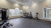 Located at 100 Alexander Xing in Loganville, GA, this fitness center is a well-designed, single-room workout facility that offers a comprehensive exercise experience. The space is architecturally distinguished by its elevated tray ceilings adorned with crown molding and recessed lighting, which together create a bright, open atmosphere that feels more expansive than a typical gym setting.

Natural light floods the room through large arched and wide rectangular windows with white shutters, offering views of the surrounding neighborhood. The neutral gray walls and durable rubber flooring provide a clean, functional backdrop suited to high-activity use.

The fitness center is equipped with a full range of exercise equipment. Cardio options include two treadmills, an elliptical trainer, and a stationary bike, all positioned to take advantage of the natural light from the windows. On the strength-training side, the space features a multi-station cable machine and a multi-functional weight system, complemented by a large wall-mounted mirror that enhances the sense of space and supports proper form during workouts.

A glass-paneled door provides secondary access to the space, adding convenience and connecting to an outdoor area. The overall design balances elegant architectural details with practical fitness functionality, making this facility a standout amenity.