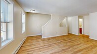 Located at 235 W Main St in downtown Stamford, Connecticut, this multi-floor residence offers two bedrooms and two bathrooms spread across three distinct levels. Light-toned hardwood flooring runs consistently throughout the home, lending a warm, cohesive aesthetic to every room.

The main living level serves as the functional heart of the home, featuring a galley-style kitchen outfitted with rich wood cabinetry, white countertops, a stainless steel sink, and white appliances including a refrigerator and range. The layout maximizes storage and counter space efficiently.

The upper floor contains the primary bedroom, a generously sized room with natural light streaming through a set of multi-pane windows and baseboard heating. A dedicated closet with wire shelving provides practical storage. The second bedroom mirrors this bright, open feel, also featuring hardwood floors and a closet. Both rooms maintain a clean, neutral palette with warm beige walls.

The two bathrooms are well-appointed: one features a full tub-shower combo with built-in shelving, warm wood vanity cabinetry, and tile flooring, while the second offers a half-bath configuration with matching finishes. Two staircases connect the floors, supporting smooth circulation throughout. The overall ambiance is clean, functional, and move-in ready.