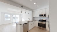 Located at The Channel Club on Waterview Road in Island Park, NY, this single-floor residence offers a clean, modern aesthetic throughout. The open-concept kitchen is outfitted with white shaker cabinetry, gray quartz countertops, a classic subway tile backsplash, and a full suite of stainless steel appliances including a gas range, over-the-range microwave, dishwasher, and refrigerator. A peninsula with pendant lighting connects the kitchen seamlessly to the living area, where sliding glass doors frame waterway views and fill the space with natural light. Light-toned hardwood-style flooring runs throughout the main living areas and bedrooms, complementing the bright white walls and recessed lighting. The bedrooms are generously sized, with large windows that invite abundant daylight; one bedroom features a tray ceiling detail. The primary bathroom is appointed with elegant marble-patterned tile flooring and a walk-in shower with a decorative mosaic tile surround. A second full bathroom provides a white vanity with a mirror and tile flooring. A convenient in-unit stacked washer and dryer is tucked within the living area. The overall ambiance is fresh, bright, and contemporary, reflecting a well-designed coastal lifestyle setting.