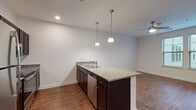 This 1-bedroom, 1-bathroom unit in Lakeland, Tennessee offers a thoughtfully designed single-floor layout with consistent, warm hardwood-style flooring running throughout. The open-concept kitchen serves as the heart of the home, centered around a large island with a granite countertop, an undermount double sink, and a stainless steel dishwasher integrated into its dark espresso cabinetry. Pendant lighting hangs above the island, adding a polished, modern touch. The kitchen is further equipped with a full suite of stainless steel appliances, including a refrigerator, range, and microwave, all complemented by matching granite countertops along the perimeter cabinetry. The kitchen flows naturally into the living area, which is fitted with a ceiling fan for year-round comfort. The bedroom is a bright and airy retreat, benefiting from dual windows that invite natural light and offer outdoor views, along with its own ceiling fan. The bathroom maintains the same design language as the rest of the unit, featuring a granite-topped dark wood vanity with a large mirror, a full soaking tub with shower, and clean white finishes throughout. Recessed lighting and crisp white walls contribute to the unit's bright, clean, and cohesive aesthetic.