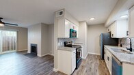 This single-floor residence offers a thoughtfully designed open layout that connects the living, dining, and kitchen areas seamlessly. The living room serves as a welcoming focal point, highlighted by a classic fireplace with a sleek surround, a ceiling fan with integrated lighting, and a large sliding glass door fitted with vertical blinds that invites natural light and provides access to an outdoor area. Wood-look plank flooring runs consistently throughout the entire unit, adding warmth and visual continuity to every room. The galley-style kitchen is well-equipped and features white shaker cabinetry, granite-look countertops, a subway tile backsplash, and a full suite of stainless steel appliances including a refrigerator, electric range, over-the-range microwave, and dishwasher. A hallway connects the main living space to the private areas of the unit, which include a generously sized bedroom with its own ceiling fan and ample closet space. The bathroom is clean and functional, outfitted with wood-look flooring, a granite vanity top, a full tub-shower combination with a curved rod, and matte black fixtures and hardware throughout. Neutral gray wall tones and a textured ceiling tie the entire space together with a cohesive, modern aesthetic.