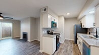 This single-floor residence offers a thoughtfully designed open layout that connects the living, dining, and kitchen areas seamlessly. The living room serves as a welcoming focal point, highlighted by a classic fireplace with a sleek surround, a ceiling fan with integrated lighting, and a large sliding glass door fitted with vertical blinds that invites natural light and provides access to an outdoor area. Wood-look plank flooring runs consistently throughout the entire unit, adding warmth and visual continuity to every room. The galley-style kitchen is well-equipped and features white shaker cabinetry, granite-look countertops, a subway tile backsplash, and a full suite of stainless steel appliances including a refrigerator, electric range, over-the-range microwave, and dishwasher. A hallway connects the main living space to the private areas of the unit, which include a generously sized bedroom with its own ceiling fan and ample closet space. The bathroom is clean and functional, outfitted with wood-look flooring, a granite vanity top, a full tub-shower combination with a curved rod, and matte black fixtures and hardware throughout. Neutral gray wall tones and a textured ceiling tie the entire space together with a cohesive, modern aesthetic.