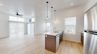 This well-designed single-floor residence offers a thoughtful layout that maximizes comfort and functionality. The open-concept kitchen and living area serves as the heart of the home, featuring light hardwood-style flooring, soaring ceilings, and abundant natural light streaming through multiple windows with outdoor views. The kitchen is appointed with warm wood-tone cabinetry, a sleek white quartz waterfall island with an integrated sink, stainless steel appliances including a refrigerator, range, and microwave, and stylish pendant lighting that adds a modern touch. The spacious living room extends naturally from the kitchen and includes a ceiling fan, recessed lighting, and sliding glass door access to a balcony. The bedroom is carpeted for comfort and is accompanied by a generously sized walk-in closet featuring built-in shelving and a hanging rod. The full bathroom mirrors the home's modern aesthetic with wood-tone cabinetry, a white quartz countertop, a large vanity mirror, and matching hardware. A dedicated laundry room rounds out the space, housing a full-size washer and dryer alongside additional built-in shelving for storage. Clean white walls and consistent finishes throughout create a cohesive, contemporary ambiance.