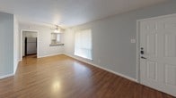 This 2-bedroom, 2-bathroom unit is laid out entirely on a single floor, offering a cohesive and easy-to-navigate living space. The open living area features warm wood-style flooring and a large vertical-blind window that brings in natural light, with a pass-through view into the adjacent kitchen. The kitchen is equipped with black appliances including a range, over-the-range microwave, and refrigerator, complemented by white cabinetry and granite-style countertops, creating a clean contrast throughout the space. Both bedrooms are generously proportioned, each featuring warm hardwood-style flooring, ceiling fans with integrated lighting, and windows with vertical blinds that provide natural light and outdoor views. One bedroom includes a sliding-door closet with built-in rod storage. The two bathrooms are finished with diagonal-set ceramic tile flooring and full tub-shower combinations surrounded by earthy square tile, with granite-style vanity countertops adding a polished touch. A dedicated living area with rich, dark wood-style flooring and a textured ceiling rounds out the unit, providing a comfortable and functional common space. Throughout, the soft gray-toned walls lend a neutral, modern ambiance that ties all areas of the unit together cohesively.