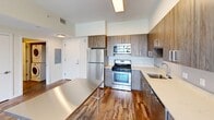 This well-appointed 3-bedroom, 1-bathroom residence in Stamford, CT offers a thoughtfully designed single-floor layout that balances comfort and modern style. Rich, multi-toned hardwood-style flooring flows throughout the living areas and bedrooms, adding warmth and character to the clean, contemporary aesthetic defined by crisp white walls and abundant natural light.

The open kitchen-living area serves as the heart of the home, featuring a fully equipped kitchen with stainless steel appliances, wood-grain cabinetry, light stone countertops, and a stainless steel island — ideal for both everyday cooking and entertaining. The adjacent living room is generously proportioned, with large floor-to-ceiling windows framing expansive views of a lush green campus, community pool, playground, and the Stamford skyline beyond.

The three bedrooms are well-sized, with the primary bedroom offering comfortable, versatile space. The full bathroom is sleekly finished with a modern floating vanity, ample counter space, and a stacked in-unit washer/dryer for added convenience. A dedicated closet provides practical storage throughout. The overall ambiance is bright, clean, and move-in ready, reflecting a modern urban lifestyle in a desirable Stamford location.