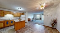 Located at 6120 Westwood Pkwy in Saint Cloud, MN, this single-floor, one-bedroom, one-bathroom unit offers a practical and comfortable layout. The open-concept kitchen and living area serves as the heart of the space, with warm oak cabinetry, a center island with breakfast bar, white appliances including a refrigerator, range, and built-in microwave, all set on durable stone-look tile flooring. The kitchen flows seamlessly into the carpeted living room, which is highlighted by a corner fireplace with a wood-trimmed surround, a ceiling fan, and large windows alongside a private exterior door that fills the space with natural light and offers views of the surrounding greenery. The bedroom features plush carpeting, a wide double-door closet, a ceiling light fixture, and a window overlooking the outdoors. The full bathroom is equipped with an oak vanity, a wide mirror with Hollywood-style lighting, and a shower/tub combination. A dedicated laundry area houses a full-sized side-by-side washer and dryer. Three closets throughout the unit provide ample storage. Textured ceilings and warm wood-toned trim details are consistent throughout, contributing to a cohesive and functional living environment.
