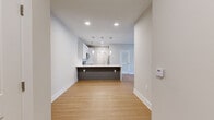 This well-appointed single-floor residence showcases a clean, modern aesthetic throughout, combining light wood-look flooring, neutral wall tones, and bright recessed lighting to create an inviting and cohesive atmosphere. The open-concept layout centers around a contemporary kitchen equipped with white shaker-style cabinetry, quartz countertops, and a full suite of stainless steel appliances including a range, microwave, dishwasher, and refrigerator. A peninsula with an integrated sink and pendant lighting above serves as a natural divider between the kitchen and the open living area, which benefits from recessed lighting and a ceiling fan overhead. The bedrooms are carpeted for comfort and feature ceiling fans, natural light from slatted-blind windows, and ample closet space, including a walk-in closet in one of the rooms. The primary bathroom is highlighted by a double-sink vanity with white cabinetry, quartz countertops, and a large wall mirror with overhead lighting. A dedicated laundry room provides full-size, side-by-side washer and dryer units with overhead wire shelving for additional storage. Throughout the unit, clean lines, white trim, and a consistent neutral palette contribute to a polished and functional living environment.