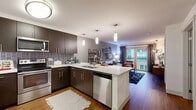 Located in the heart of Bellevue, WA, Unit 607 at 10595 Main St offers a thoughtfully designed single-floor layout that balances modern style with everyday functionality. The open-concept kitchen is a standout feature, showcasing rich dark cabinetry, a textured tile backsplash, light quartz countertops, and a full suite of stainless steel appliances including a refrigerator, range, microwave, and dishwasher. A central island with bar seating and elegant pendant lighting makes the kitchen equally suited for casual dining and entertaining. Warm hardwood-style flooring flows seamlessly throughout the main living areas. The living room is bright and welcoming, anchored by a large sliding glass door that opens to a private balcony with views of the surrounding Bellevue streetscape, allowing generous natural light to fill the space. The bedroom is a serene retreat featuring plush carpeting, a sliding door to an additional outdoor area, and a soothing color palette. The full bathroom connects conveniently to the bedroom and includes a soaking tub, dark vanity cabinetry, and hardwood-style flooring. Throughout the unit, neutral tones and clean architectural lines create a cohesive, contemporary ambiance well-suited to urban living in downtown Bellevue.