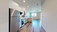 This thoughtfully designed single-floor unit offers a clean, modern aesthetic with an efficient and functional layout. Light wood-tone flooring runs continuously throughout the space, lending warmth and visual cohesion to every room.

The open-concept kitchen is a standout feature, outfitted with sleek white upper cabinetry, warm wood-toned lower cabinets, and a full suite of stainless steel appliances including a refrigerator, range, microwave, and dishwasher. A gray subway tile backsplash adds a contemporary touch, while a peninsula provides additional counter space and defines the boundary between the kitchen and the living area. Recessed lighting and a pendant light above the peninsula ensure ample illumination, and a ceiling fan in the living area promotes comfortable airflow.

Large windows in the living area flood the space with natural light and frame views of the surrounding landscape, creating a bright and airy atmosphere. The living area is open and versatile, offering a generous canvas for various furniture arrangements.

The bathroom is finished in a clean, minimalist style with a white vanity, mirror, and wood-look tile flooring consistent with the rest of the unit. A louvered closet door provides access to dedicated storage. The entrance corridor provides a clear and functional transition into the main living spaces, completing this well-appointed modern unit.