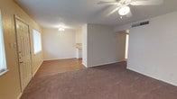 This single-story property at 502 Slide Rd in Lubbock, Texas offers a straightforward, functional layout with consistent finishes throughout. The living area serves as a central gathering space, highlighted by a corner fireplace with a white wood-paneled surround and a classic mantel, providing a focal point for the room. A ceiling fan with a light fixture is mounted to the textured ceiling, promoting air circulation. Plush wall-to-wall carpeting in a warm brown tone runs throughout the living area and extends into the bedrooms, adding comfort underfoot. The bedrooms are well-proportioned, each featuring ceiling fans, textured ceilings, and large windows fitted with horizontal blinds that allow for natural light while maintaining privacy. The walls feature a mix of painted drywall and panel-style sections, giving each room a distinct character. The warm, neutral color palette of yellows and whites used throughout creates a cohesive and inviting atmosphere. Overall, the property presents a practical and comfortable single-floor living environment suited for a variety of occupants.