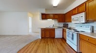 This single-floor residence at 1680 Deer Creek Dr in Xenia, Ohio, offers a thoughtfully designed layout with a seamless flow between living, dining, and kitchen spaces. The kitchen is a standout feature, showcasing warm oak cabinetry that extends to the ceiling for generous storage, light countertops, and a full suite of white appliances including a range, built-in microwave, dishwasher, and refrigerator. Durable hardwood-style flooring anchors the kitchen and transitions into the living areas. The open living room is generously proportioned, finished with plush neutral carpeting and illuminated by flush-mount lighting, with a pass-through peninsula connecting it to the kitchen. Two well-sized bedrooms feature soft carpet, natural light from windows with outdoor views, and closet storage. The unit includes two bathrooms, each finished with warm tile flooring, oak vanity cabinetry, and tub/shower combinations with curtain enclosures. A dedicated closet area adjacent to the main living space provides additional storage. The overall design presents a clean, neutral palette throughout, offering a comfortable and functional living environment in a residential Xenia neighborhood.