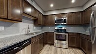 Located at 890 Tallmadge Rd in Kent, Ohio, this single-floor residence offers a well-designed layout with modern finishes throughout. The kitchen is a standout feature, showcasing rich dark wood cabinetry, granite countertops, a subway tile backsplash, and a full suite of stainless steel appliances including a range, over-the-range microwave, dishwasher, and refrigerator. Light wood-tone luxury vinyl plank flooring runs through the kitchen and main living areas, lending a warm, cohesive feel to the space. The open living and dining area is generously sized, with neutral gray walls, recessed lighting, and ceiling fans that enhance both comfort and functionality. Large windows dressed with horizontal blinds allow natural light to filter into the bedrooms, each of which features plush wall-to-wall carpeting and ample closet space. The primary bedroom includes a walk-in closet and direct access to an en-suite bathroom. Both bathrooms are finished with dark wood vanities, granite countertops, undermount sinks, and wood-look vinyl flooring, maintaining a consistent and polished aesthetic throughout the home.
