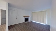 This single-floor unit offers a clean, modern aesthetic with a neutral color palette throughout. The living room serves as a welcoming focal point, showcasing a tile-surround fireplace accented by a rustic wood mantel, warm wood-look laminate flooring, and a large sliding glass door covered by vertical blinds that allows natural light to fill the space.

The layout transitions smoothly into a dining and kitchen area, where an open-concept peninsula with white countertops separates the two spaces. The kitchen is well-appointed with gray cabinetry, white subway tile backsplash, stainless steel appliances including a refrigerator, range, microwave, and dishwasher, as well as a deep stainless steel sink with a modern pull-down faucet. Wood-look laminate flooring continues throughout these areas, contributing to a cohesive feel.

The bedroom features plush carpet flooring and a window fitted with horizontal blinds, providing natural light and privacy. The bathroom includes a tiled shower-tub combination, a gray vanity with a white countertop, and wood-look flooring that ties in with the rest of the unit. Overall, the space presents a fresh, well-maintained interior with contemporary finishes.
