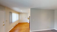 This single-floor unit offers a practical and well-organized layout across several distinct living areas. The living room is bright and welcoming, featuring warm hardwood flooring, a large window dressed with sheer white curtains that allow natural light to filter through, and a baseboard heating unit. Recessed lighting overhead adds a clean, modern touch to the space. Adjacent to the living area, the galley-style kitchen is well-appointed with crisp white shaker cabinetry extending to the ceiling on both sides, offering generous storage. Granite countertops with warm gold and brown tones complement the stainless steel refrigerator and white range, while hardwood floors and recessed lighting complete the polished look. A separate carpeted area transitions toward the bedroom, which features soft, neutral-toned carpet, light gray walls, and a textured ceiling, creating a calm and comfortable atmosphere. The full bathroom includes a tub and shower combination enclosed by sliding frosted glass doors, a single-sink vanity with a mirrored medicine cabinet, and a small window that provides ventilation and natural light. Throughout the unit, a consistent neutral color palette of soft grays and warm beiges creates a cohesive and move-in ready environment.