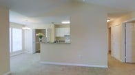 Located at 1525 E Pass Rd in Gulfport, Mississippi, this single-floor home offers a clean, open-concept layout designed for comfortable everyday living. The living area is defined by soaring vaulted ceilings that lend a sense of spaciousness and airiness to the space, with soft neutral wall tones and plush carpeting underfoot contributing to a warm, inviting atmosphere. A defining architectural feature is the kitchen pass-through, which seamlessly connects the living area to the kitchen, making the space feel expansive and well-integrated. The kitchen is equipped with white cabinetry providing ample storage, a granite-style countertop along the breakfast bar, and standard appliances including a range. Under-cabinet lighting adds functionality to the workspace. Adjacent to the kitchen, a hallway leads to additional rooms, hinting at a thoughtful and practical floor plan. Large doorways and consistent neutral finishes throughout create a cohesive and welcoming environment. The home's single-story design ensures easy accessibility throughout, while the overall layout balances open communal spaces with more private areas, making it a functional and comfortable residence in the Gulfport, MS area.