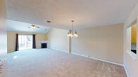 This two-floor home offers a well-considered layout with a range of functional and comfortable living spaces throughout. The main living area is immediately impressive, featuring soaring vaulted ceilings accented by a ceiling fan and an elegant chandelier, all anchored by a classic fireplace set against neutral-toned walls and soft wall-to-wall carpeting. Natural light filters in through a sliding glass door, enhancing the open and airy atmosphere.

The kitchen is efficiently designed with warm oak cabinetry, dark laminate countertops, hardwood flooring, and stainless steel appliances including a built-in microwave and dishwasher. A pass-through opening connects the kitchen directly to the living area, promoting an open-concept flow ideal for everyday living and entertaining.

The upper level includes generously sized bedrooms with vaulted ceilings, plush carpeting, and ample natural light. The primary bedroom provides access to a dedicated bathroom and a walk-in closet. Bathrooms throughout are cleanly appointed with wood-toned vanities and hardwood-style flooring.

A dedicated laundry room with a utility sink, wire shelving, and washer/dryer hookups adds everyday convenience. The attached two-car garage features a concrete floor and an automatic opener, completing this practical and comfortable home.