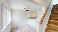 This two-story, 2-bedroom, 1-bathroom home is thoughtfully laid out across two levels, offering a clean, bright aesthetic throughout. The main floor features light-toned hardwood flooring and an open living area centered around a ceiling fan. The kitchen is well-appointed with white cabinetry, a subway tile backsplash, ample countertop space, and a peninsula that doubles as a breakfast bar. A gas range, refrigerator, and double sink complete the functional kitchen setup. A wood-railed staircase leads to the upper level, where both bedrooms are finished with plush wall-to-wall carpeting and neutral white walls. The spacious primary bedroom features vaulted ceilings, multiple windows for natural light, and generous closet space with built-in shelving. The second bedroom is bright and airy, with dual windows offering outdoor views. A hallway connects the upper-level rooms and provides access to the full bathroom, which features white square tile with a contrasting dark accent border and a tub/shower combination with matte black hardware. A dedicated closet and hallway provide additional storage throughout. The home presents a clean, move-in-ready interior with a cohesive, light-filled design.