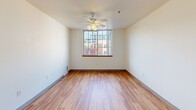 Located at 920 NW Kearney St in Portland, Oregon, this efficiently laid-out unit offers a thoughtful use of space across a single floor. The combined living and dining area serves as the heart of the home, featuring light hardwood-style flooring, neutral white walls, and a ceiling fan with built-in lighting. A large window floods the room with natural light and provides views of the surrounding urban neighborhood, creating a bright and inviting atmosphere. The kitchen is well-appointed with warm wood-trimmed cabinetry, white upper and lower cabinet doors, a dual-basin sink, a range with cooktop, and a full-size refrigerator — all arranged along a single efficient wall with a peninsula counter offering additional prep space. The bathroom features the same light hardwood flooring, a single-basin vanity with ample counter space, a toilet, and a full bathtub with a grab bar, enclosed by warm wood-toned doors. The bedroom is carpeted for comfort, offering a quiet retreat with a window that lets in natural light. Two closets provide generous storage, including one with built-in adjustable shelving. The entrance hallway connects all areas smoothly, with clean finishes and wood-toned doors consistent throughout the unit, lending a cohesive, warm aesthetic.