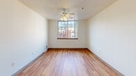 Located at 920 NW Kearney St in Portland, Oregon, this efficiently laid-out unit offers a thoughtful use of space across a single floor. The combined living and dining area serves as the heart of the home, featuring light hardwood-style flooring, neutral white walls, and a ceiling fan with built-in lighting. A large window floods the room with natural light and provides views of the surrounding urban neighborhood, creating a bright and inviting atmosphere. The kitchen is well-appointed with warm wood-trimmed cabinetry, white upper and lower cabinet doors, a dual-basin sink, a range with cooktop, and a full-size refrigerator — all arranged along a single efficient wall with a peninsula counter offering additional prep space. The bathroom features the same light hardwood flooring, a single-basin vanity with ample counter space, a toilet, and a full bathtub with a grab bar, enclosed by warm wood-toned doors. The bedroom is carpeted for comfort, offering a quiet retreat with a window that lets in natural light. Two closets provide generous storage, including one with built-in adjustable shelving. The entrance hallway connects all areas smoothly, with clean finishes and wood-toned doors consistent throughout the unit, lending a cohesive, warm aesthetic.
