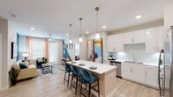 This thoughtfully designed single-floor residence offers a seamless blend of modern aesthetics and functional living. The open-concept kitchen is a standout feature, showcasing crisp white cabinetry extending to the ceiling, a full suite of stainless steel appliances, a white quartz countertop island with seating for multiple guests, and stylish pendant lighting overhead. Light wood-tone flooring runs throughout the main living areas, enhancing the bright, airy atmosphere created by recessed lighting and natural light from large windows.

The living area flows naturally from the kitchen, anchored by a bold teal accent wall and ceiling fan, with a glass-panel door providing additional natural light and outdoor access. The bedrooms are carpeted for comfort, each featuring ceiling fans, natural light through blinds-fitted windows with warm curtains, and ample space for furnishings.

Both bathrooms are finished in a clean, modern style with white cabinetry, quartz countertops, and light wood flooring. One bathroom features a double-sink vanity with a large mirror and direct access to a well-organized walk-in closet with built-in shelving and hanging storage. The overall ambiance throughout is contemporary, cohesive, and move-in ready.