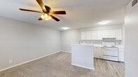 This single-floor, 3-bedroom, 1-bathroom home is thoughtfully laid out to maximize functionality within a compact footprint. The open-concept living and kitchen area serves as the heart of the home, where light gray walls and a textured ceiling set a clean, neutral backdrop. A ceiling fan with a built-in light fixture provides both comfort and illumination to the living space, which features soft carpeting that transitions to wood-look vinyl flooring in the kitchen. A peninsula with a built-in sink divides the two areas, offering casual seating or prep space. The kitchen is well-appointed with crisp white cabinetry, white appliances including an electric range, dishwasher, and refrigerator, and ample counter space. The three bedrooms are carpeted and finished with the same neutral tones, each offering a calm and versatile space. One bedroom includes a closet with wire shelving for organized storage, while another features a dedicated closet with sliding panel doors. The bathroom includes a full tub-shower combo with brushed nickel fixtures and wood-look tile flooring. A hallway and additional closet complete the layout, providing practical storage solutions throughout the home.