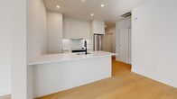 Located on the prestigious Rue Sherbrooke Ouest in Montréal, this modern 2-bedroom, 2-bathroom residence offers a thoughtfully designed single-floor layout with clean architectural lines and a crisp, contemporary aesthetic throughout. Light-toned hardwood flooring flows seamlessly across the entire space, complementing the all-white palette that maximizes brightness and openness.

The open-concept living and kitchen area serves as the heart of the home, anchored by a sleek island with white quartz countertops and a matte black faucet. The kitchen features handle-free cabinetry extending to the ceiling, stainless steel appliances, and a built-in oven. A striking gold pendant light adds a warm focal point above the island. An expansive bank of black-framed floor-to-ceiling windows floods the living area with natural light and frames views of the surrounding Montréal cityscape.

Both bedrooms are bright and serene, with one featuring a large window overlooking mature trees. The second bedroom includes a sliding panel closet. Each bathroom is finished in warm beige tile with white floating vanities, matte black fixtures, and full glass-enclosed walk-in showers with sliding barn-style doors. A stacked in-unit Whirlpool washer and dryer adds everyday convenience. The overall ambiance is modern, minimalist, and refined.