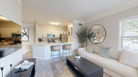 This thoughtfully designed single-floor residence offers a cohesive and functional layout encompassing a kitchen, dining room, living room, bedroom, bathroom, pantry, laundry, two closets, a hallway, and an entrance. The open-concept living and dining area flows seamlessly into the kitchen, which features white shaker cabinetry with black hardware, stainless steel appliances including a refrigerator, microwave, and electric range, light quartz countertops, tile flooring, and a peninsula with bar seating — ideal for casual dining or entertaining. The living room is bright and welcoming, with multiple windows that invite natural light, crown molding, neutral carpet, and a clean, contemporary aesthetic. The bedroom is a comfortable retreat with carpet flooring, a natural light-filled window, and access to two closets, providing ample storage. The full bathroom includes a tub-shower combination with white tile surround. A dedicated laundry area adds everyday convenience. Throughout the residence, a neutral warm-gray and white color palette, consistent trim work, and an efficient use of space contribute to a cohesive and comfortable living environment suited for a variety of lifestyles.