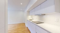 Located at 3455 Rue Aylmer in Montréal's lively Milton-Parc neighbourhood, this efficiently designed single-floor studio offers a clean, contemporary aesthetic throughout. The open-plan living and kitchen area is anchored by warm hardwood flooring that runs the full length of the space, contrasting beautifully with crisp white walls and recessed ceiling lighting that keeps the interior bright and airy. A sliding window allows natural light to filter in and provides a view onto the surrounding streetscape.

The kitchen is thoughtfully integrated along one wall, featuring sleek flat-front cabinetry finished in soft grey-white tones, a black induction cooktop, a stainless steel under-mount sink with a modern faucet, a built-in oven, and an overhead range hood. Generous upper cabinetry maximizes storage without compromising the open feel of the space. A wall-mounted electric heater ensures year-round comfort.

The bathroom is finished to a high standard, clad in large-format taupe tiles from floor to mid-wall. It includes a wall-hung white vanity with a sleek basin, a toilet, and a glass-enclosed shower, all complemented by a large mirror and chrome towel bar. The overall design of this studio prioritizes clean lines, functional use of space, and a neutral palette that offers a versatile, move-in-ready environment.