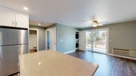 This single-floor residence in Livermore, California offers a thoughtfully designed open-concept layout with consistent soft sage-green walls and wood-style flooring throughout the main living areas. The kitchen serves as the heart of the home, showcasing crisp white shaker cabinetry with brushed nickel hardware, stone-finish countertops, a full suite of stainless steel appliances including a refrigerator, range, microwave, and dishwasher, and a central island that provides additional prep space and flows seamlessly into the living area. Recessed lighting brightens the kitchen, while a window above the sink allows natural light to filter in. The spacious living area features dark hardwood-style flooring, a ceiling fan with light fixture, and a wall-mounted AC unit. A sliding glass door opens directly to a private balcony with views of mature trees. Conveniently tucked into the living space is an in-unit stacked washer and dryer. The bedroom is carpeted and bright, with a ceiling fan and a window that brings in natural light. The bathroom is clean and functional, featuring a tub-shower combination, a white vanity with stone countertop, and wood-style tile flooring. A walk-in closet adds practical storage to the layout.
