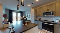 This single-floor residence showcases a thoughtfully designed open-concept layout that seamlessly connects the kitchen and living areas. The kitchen is a standout feature, outfitted with sage-toned shaker-style cabinetry, dark quartz countertops, a herringbone tile backsplash, and a full suite of stainless steel appliances including a gas range, microwave, and refrigerator. A central island with an undermount sink and matte black faucet serves as a functional focal point, with geometric pendant lighting suspended above. Light wood-style flooring runs throughout the kitchen and flows into the open living area, where large French doors with horizontal blinds and dark curtain panels invite natural light and provide views of the surrounding cityscape. The living space is defined by its clean lines and modern aesthetic, offering a welcoming and versatile layout. The bedroom is a comfortable retreat, featuring a ceiling fan, large windows overlooking the exterior, and soft carpeting underfoot. The bathroom is generously proportioned, with large-format floor tiles, a dual-sink vanity with wood cabinetry and dark hardware, a walk-in shower with white subway tile, and a separate water closet. Together, these spaces deliver a cohesive, contemporary living experience with quality finishes at every turn.