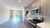 Located at 5401 Atlantic Springs Rd in Raleigh, NC, this single-floor unit showcases a contemporary design with consistent wood-look luxury vinyl plank flooring throughout. The open-concept layout connects the kitchen and living area seamlessly, creating a bright, cohesive living environment.

The kitchen is a standout feature, equipped with a full suite of stainless steel appliances, including a range, microwave, dishwasher, and refrigerator. Warm-toned wood-grain cabinetry extends from floor to ceiling, complemented by a grey subway tile backsplash and light quartz countertops. A sliding glass door in the living area opens to a private balcony overlooking a wooded backdrop, filling the space with natural light.

The bedrooms are well-proportioned, each featuring ceiling fans and windows that invite additional natural light. Closet space is generous, with wire shelving systems providing organized storage.

The bathroom is finished with a large walk-in shower clad in white subway tile and framed by a sliding glass door, paired with a wood-grain vanity and white countertop that mirrors the kitchen's design language. The overall palette of soft greys, warm wood tones, and white accents gives the unit a clean, modern, and cohesive aesthetic throughout.