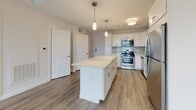 Located at 674 Dartmouth Street in Dartmouth, Massachusetts, this well-appointed single-floor residence offers a thoughtfully designed layout with clean, contemporary finishes throughout. The open-concept living and kitchen area is anchored by smooth hardwood-style flooring and filled with natural light from large, slatted windows. The kitchen is a standout feature, outfitted with crisp white shaker cabinetry, quartz countertops, a subway tile backsplash, glass shelving accents, stainless steel appliances including a gas range, dishwasher, and refrigerator, and a central island with pendant lighting — ideal for both cooking and casual dining. The living area flows seamlessly from the kitchen, providing a bright, versatile space. The bedrooms are generously proportioned, finished with plush neutral carpeting and large windows that invite ample natural light, including one corner bedroom with dual-window exposure. The bathrooms are finished with light stone-look tile flooring, white cabinetry with quartz surfaces, and brushed nickel hardware, with accessibility-friendly grab bars incorporated into the design. The unit's neutral color palette and modern detailing create a clean, cohesive aesthetic throughout.