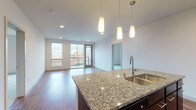 Located at 704 Williamson Street in Madison, WI, this single-floor unit offers a thoughtfully designed open-concept layout with contemporary finishes throughout. The kitchen serves as a central focal point, featuring granite countertops, dark cabinetry, stainless steel appliances including a refrigerator, range, and built-in microwave, and a large island with a stainless steel sink. Pendant lighting illuminates the island, while recessed lighting carries throughout the main living area. Hardwood-style flooring extends across the kitchen and living spaces, which open directly onto a private balcony offering views of the surrounding Madison neighborhood. The bedroom is carpeted and features a ceiling fan, a generous walk-in closet with wire shelving, and a large window that brings in ample natural light. Two bathrooms serve the unit — one with a sleek glass-enclosed shower and dark vanity, and another with a full tub-shower combination and light tile flooring. A dedicated laundry area houses a stacked washer and dryer. The overall aesthetic is clean and modern, with a neutral palette, crisp white walls, and consistent finishes that create a cohesive, contemporary ambiance throughout.