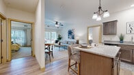 This single-floor residence offers a thoughtfully designed open-concept layout that seamlessly connects the kitchen, dining, and living areas. The kitchen is outfitted with dark wood cabinetry, granite countertops, stainless steel appliances including a refrigerator, range, and microwave, and light hardwood-style flooring that extends throughout the main living spaces. A breakfast bar with pendant lighting provides an additional casual dining option.

The living and dining area is bright and welcoming, anchored by a ceiling fan and large sliding glass doors that open to an outdoor view, allowing generous natural light to fill the space. The open layout comfortably accommodates both a dining set and a full living room arrangement.

The bedroom features plush carpeting, a sliding closet, and a window with an exterior view, creating a calm and restful retreat. A well-appointed bathroom includes a wood-toned vanity, framed mirror, and hardwood-style flooring. The dedicated laundry room houses a full-sized washer and dryer alongside overhead shelving, adding practical convenience. Throughout, the design balances neutral tones with warm wood accents, creating a cohesive and inviting ambiance across every room.