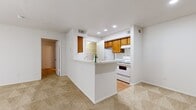 This single-floor residence offers a thoughtful layout that maximizes functionality across its five distinct areas. The combined kitchen and living room serves as the heart of the home, featuring a peninsula-style breakfast bar that separates the kitchen from the carpeted living area. The kitchen is equipped with warm-toned wood cabinetry, white appliances including an electric range and refrigerator, light stone countertops, and recessed lighting overhead. Wood-look flooring runs through the kitchen, adding a clean contrast to the carpeted living space.

The dedicated entrance provides a welcoming transition into the home. The bedroom is a comfortable, well-proportioned room with soft carpeting, a ceiling fan with light fixture, a window with blinds allowing natural light, and a large sliding glass door fitted with vertical blinds. A closet with built-in shelving is accessible from the kitchen area, offering practical storage.

The bathroom is finished with wood-look flooring, warm wood cabinetry beneath a wide vanity mirror, a light stone countertop with a single sink, and a full tub-shower combo with white tile surround. Throughout the residence, a neutral color palette of white walls and beige carpet creates a clean, cohesive ambiance well-suited for comfortable everyday living.
